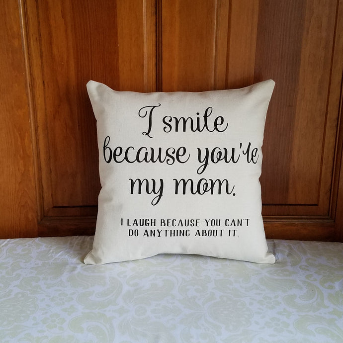 canvas pillow that reads I smile because you're my mom. I laugh because you can't do anything about it in black font, leaning against a wooden door 