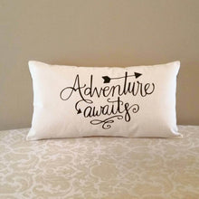 Adventure Awaits pillow leaning against a tan colored wall