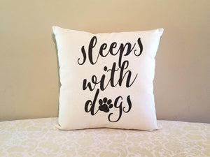 sleeps with dogs, decorative dog mom pillow, leaning against a tan wall