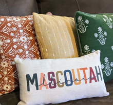 customizable city and state colorful lumbar pillow, sitting in front of three other colorful pillows on a brown couch