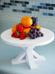 A white Farmhouse Table Cake Stand with Shiplap top that has fruit sitting on it, standing on a blue counter