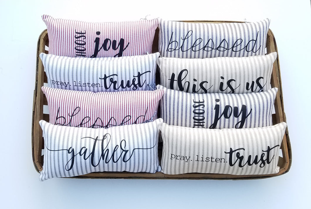 eight Mini Ticking Striped Farmhouse Pillows all sitting a a woven basket 
