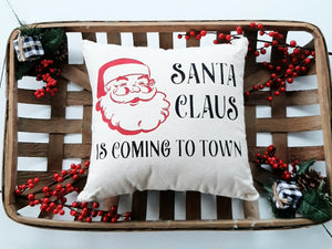 Santa Claus is coming to town decorative Christmas pillow sitting inside a woven basket decorated with red holiday berries 