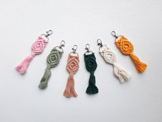 Assorted colors of boho macrame tassel keychains on a grey and white striped background 