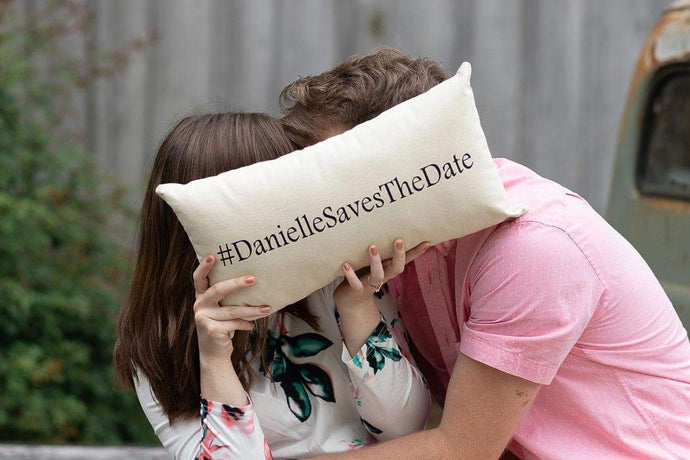 man and women kissing behind a custom wedding hashtag pillow 