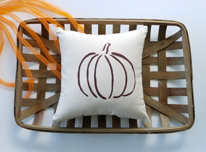 Rustic Pumpkin pillow sitting in a woven basket decorated with orange ribbon