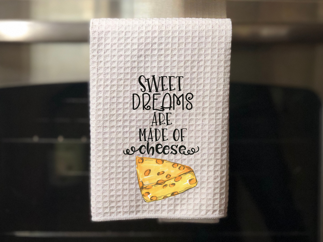 white towel with a yellow slice of Swiss cheese painted on it that reads sweet dreams are made of cheese in black font, hanging from an oven door