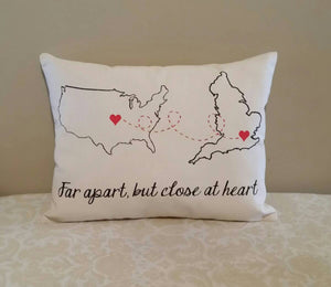 customizable far apart, but close at heart - Country to Country pillow, leaning against a tan wall