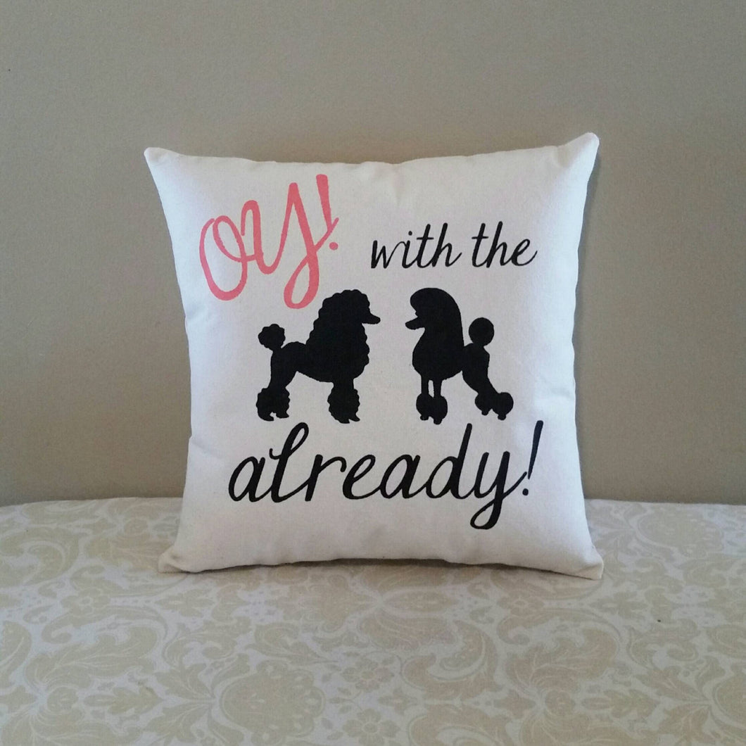 Canvas pillow that reads Oy! with the already! with two outlines of poodle dogs. leaning against a brown wall