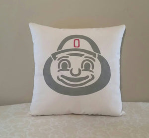 Brutus buckeye pillow leaning against a tan wall