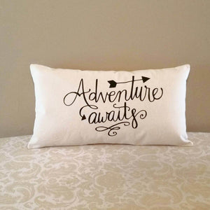 Adventure Awaits pillow leaning against a tan colored wall