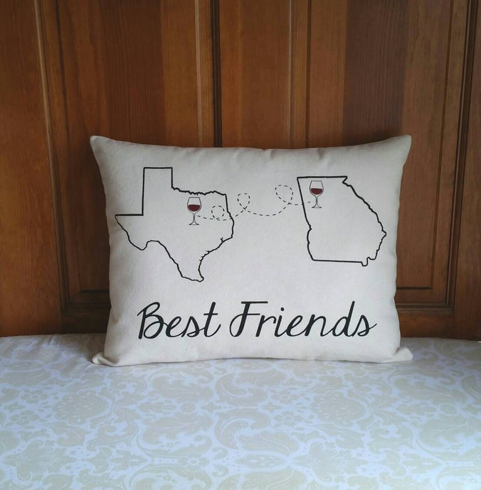 best friends pillow with two different custom states on it and wine glasses marking city locations in those states - connected by a dotted line. leaning against a wooden door