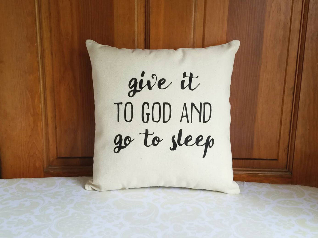 Canvas pillow with black font that reads give it to God and go to sleep. leaning against a wooden door 