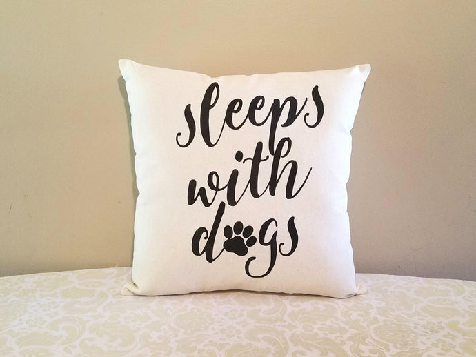 sleeps with dogs, decorative dog mom pillow, leaning against a tan wall