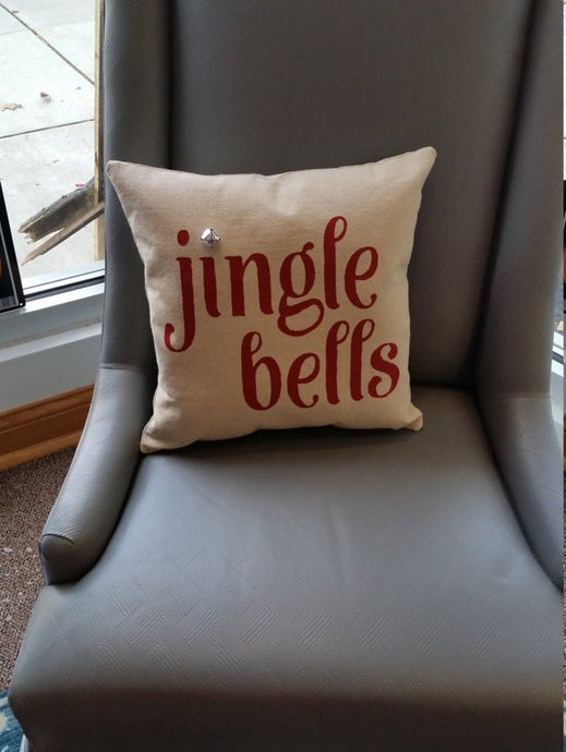 Jingle Bells Christmas pillow sitting on a grey chair