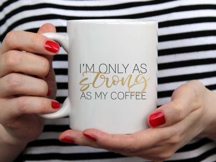 hands with red nail polish holding a white mug that reads I'm only as strong as my coffee