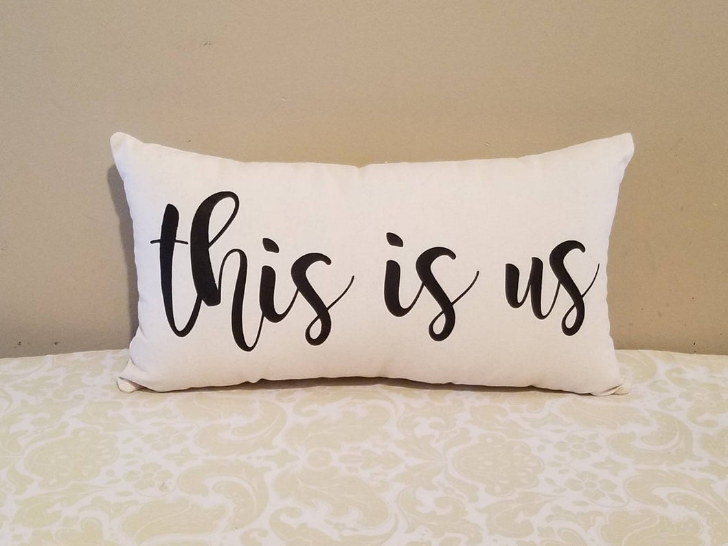 This is us modern farmhouse pillow, leaning against a tan wall
