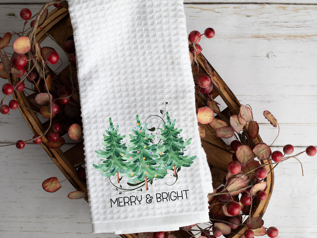 Watercolor Christmas Tree Trio and reads Merry & Bright Tea Towel, laying across a basket with berries